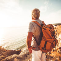 Older male overlooking the ocean with a backpack on his back / myHMB Blog & Fitness Community