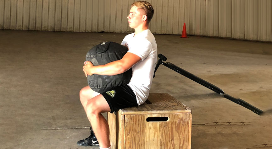 SMSU male wrestling athlete performing sandbag squats to a wooden box