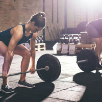 a male and female athlete deadlifting barbells in a gym