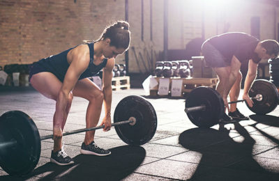 a male and female athlete deadlifting barbells in a gym