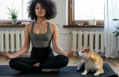 woman sitting on a yoga mat in her apartment cross legged, eyes shut, meditating and dog sitting next to her | myHMB Blog the power of meditation by Jennifer Dietrick