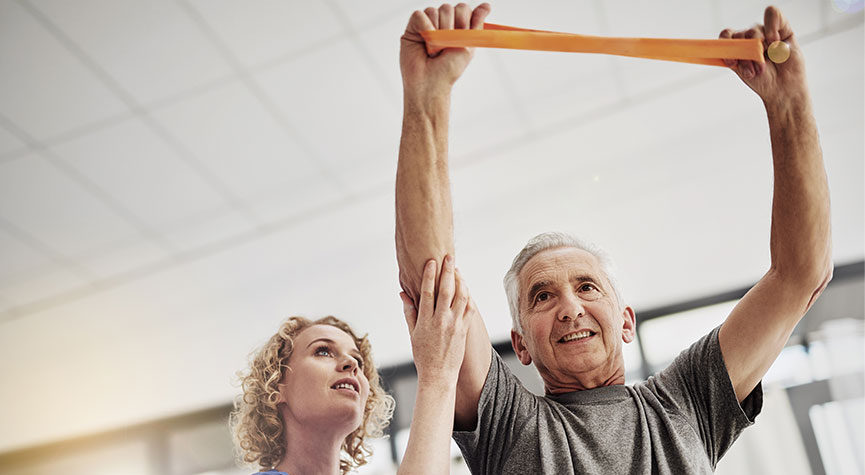 older male adult holding a resistance band overhead while working with a female pt