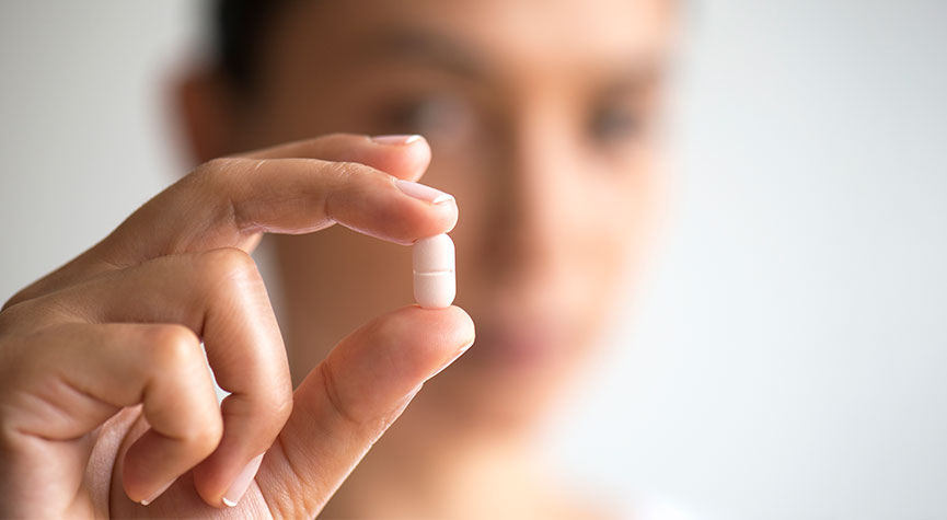 blurred woman with hand in focus holding a white pill/tablet in between her fingers