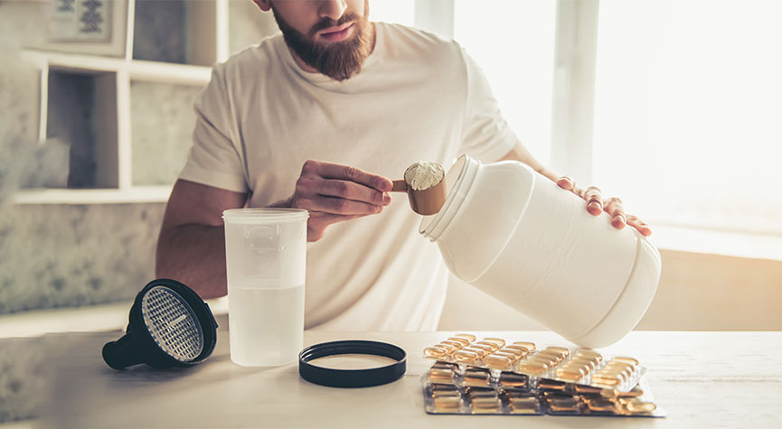 guys scooping out protein powder to make a shake and supplements on the table