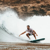 man surfing the waves with rocks in the background | myHMB news section mitigating muscle soreness