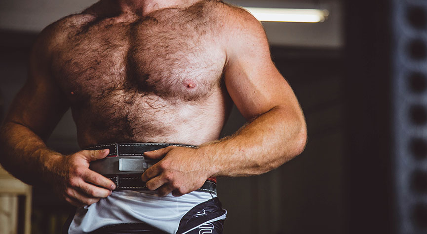 athletic man in a gym without his shirt on putting on a weightlifting belt