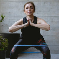 older woman with an exercise band around her thighs performing a squat | myHMB blog strength training as you age