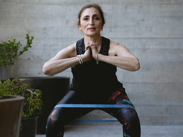 older woman with an exercise band around her thighs performing a squat | myHMB blog strength training as you age
