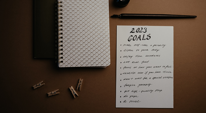 top of a desk view with a notebook, pen, and paper stating goals for 2023