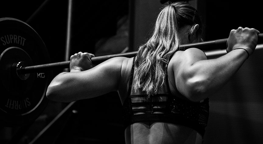 female athlete in a gym with a barbell on her back about to perform a backsquat