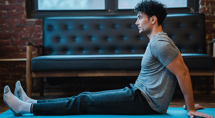 athletic male sitting on a yoga mat in his living room stretching