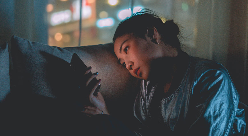 woman sitting on her couch at night looking at her cell phone
