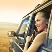 cheerful woman looking out the passenger window while driving through nature
