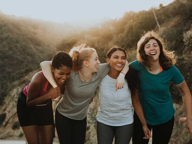 a group of diverse women outdoors walking through nature and laughing and smiling