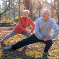 an older man and woman in a park outside stretching and doing yoga