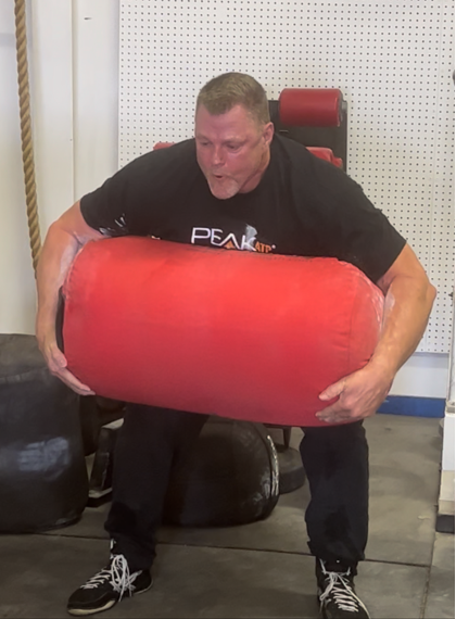 Renowned Hall of Fame powerlifter Brad Gillingham demonstrates exceptional strength and technique as he flawlessly executes a sandbag clean during a training session. The image showcases the precision and power inherent in elite powerlifting performance.